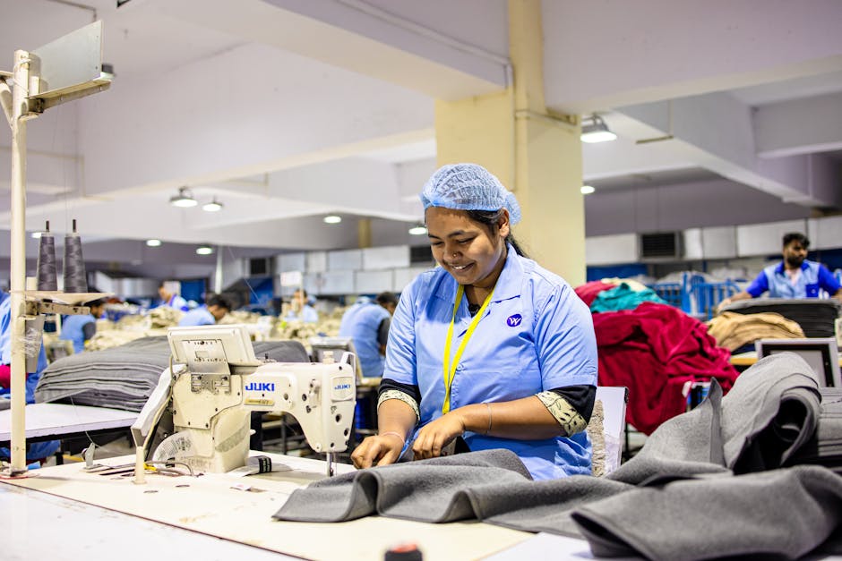 Female textile worker uses sewing machine in a busy factory setting.