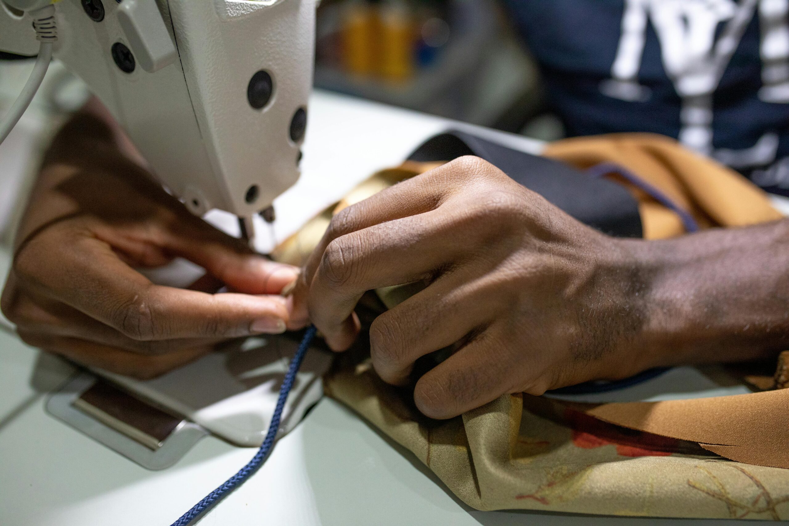 Detailed photograph of hands guiding fabric through a sewing machine, showcasing skill and craftsmanship.